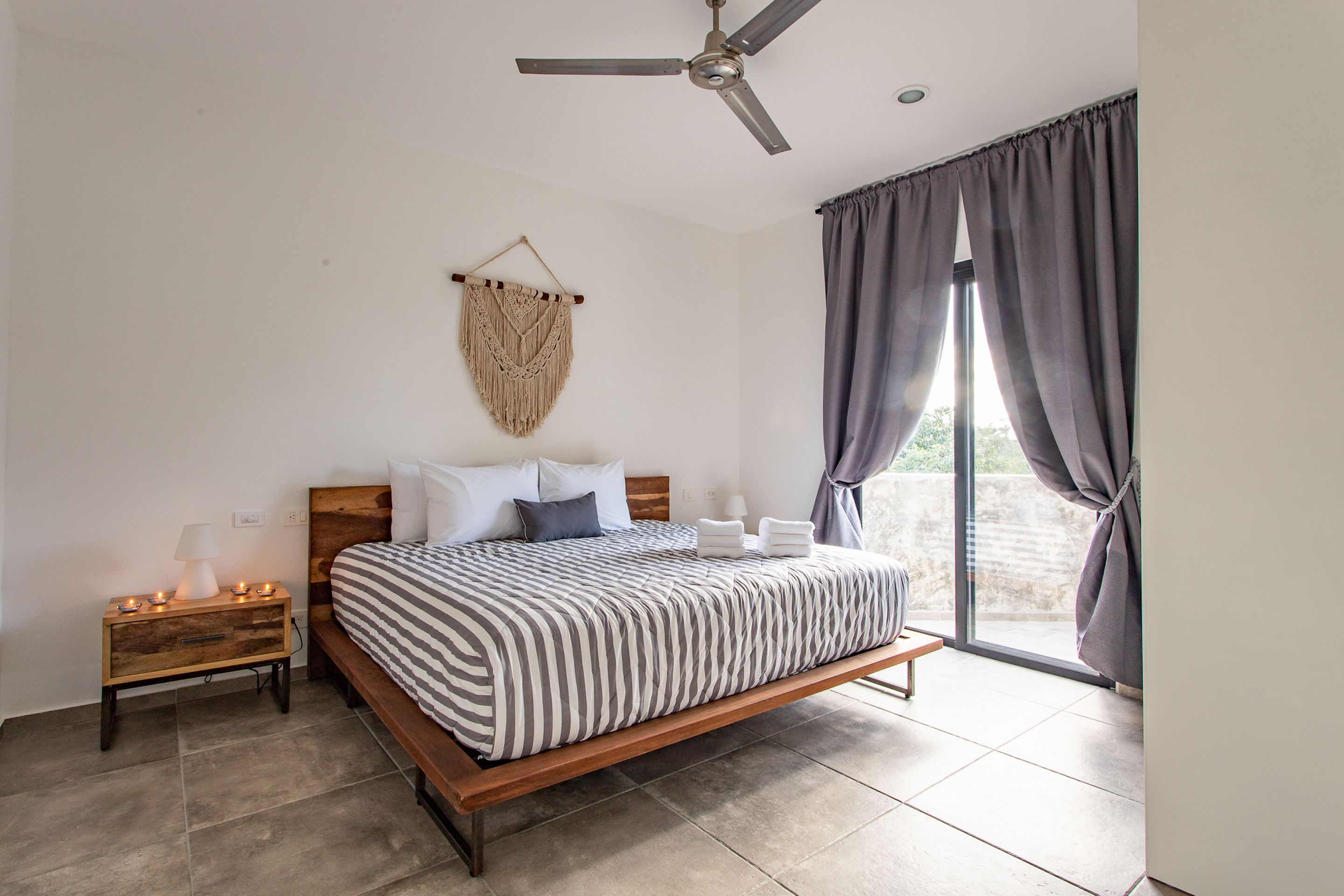 A bedroom with a bed, bedside table, lamp, and a macrame wall hanging.