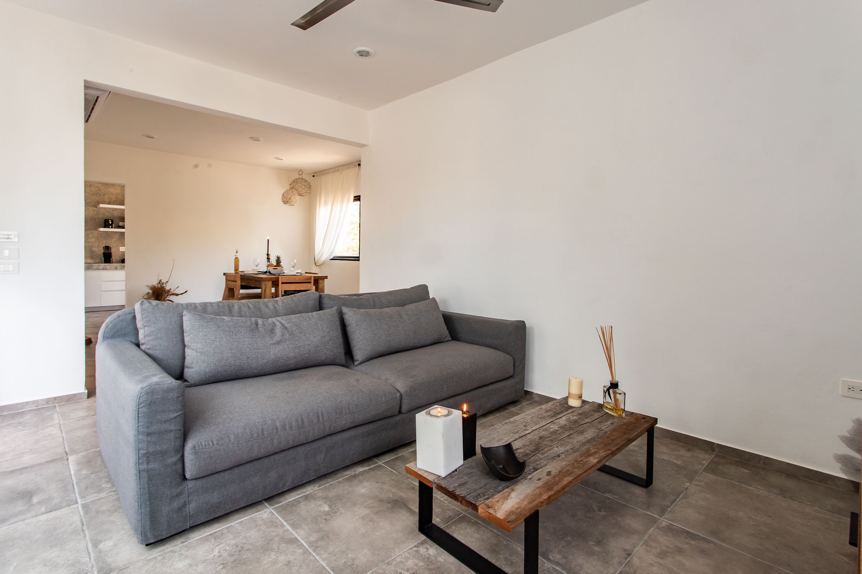 A modern living room with a grey sofa, a wooden coffee table, and a dining area in the background.