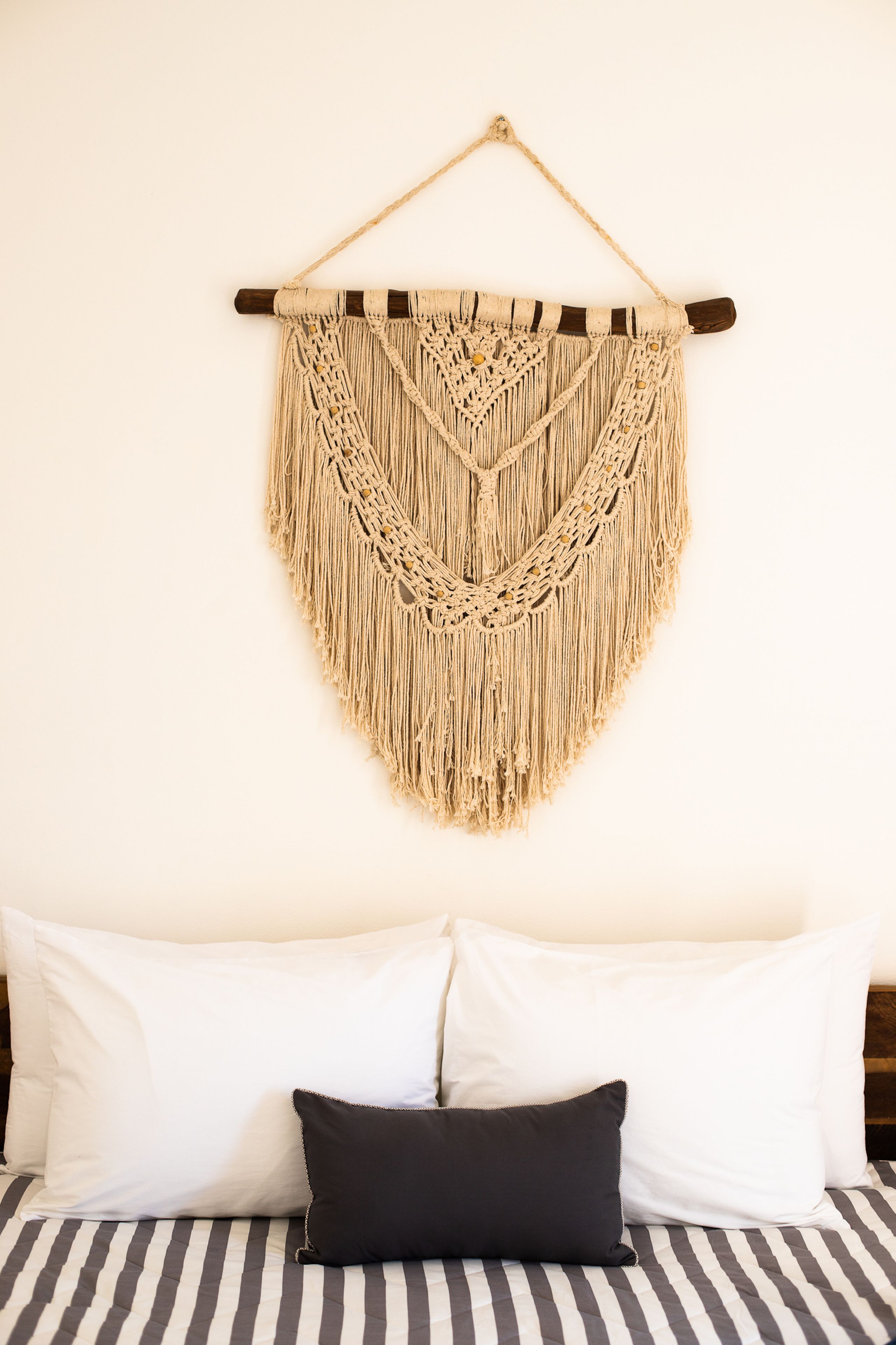 Un lit avec une literie à rayures et une décoration murale en macramé.