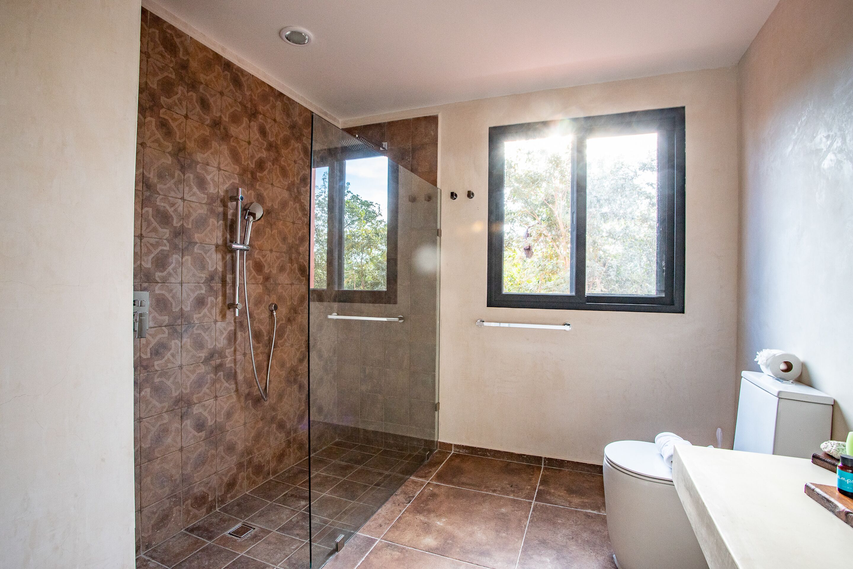A bathroom with a glass-enclosed shower, a toilet, and a window providing natural light.