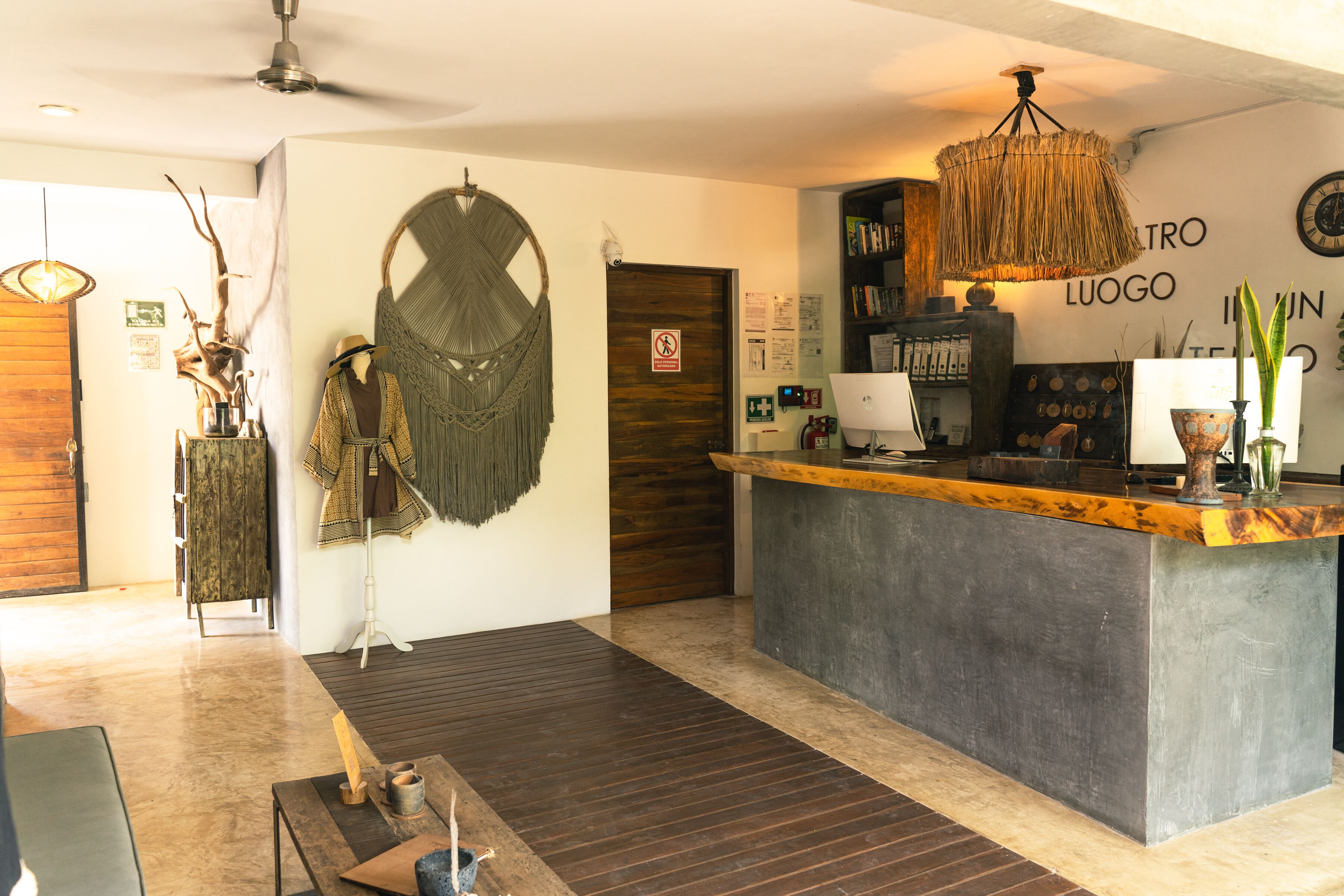 A reception area with a wooden counter, a hanging woven light fixture, and a wall-mounted clock.