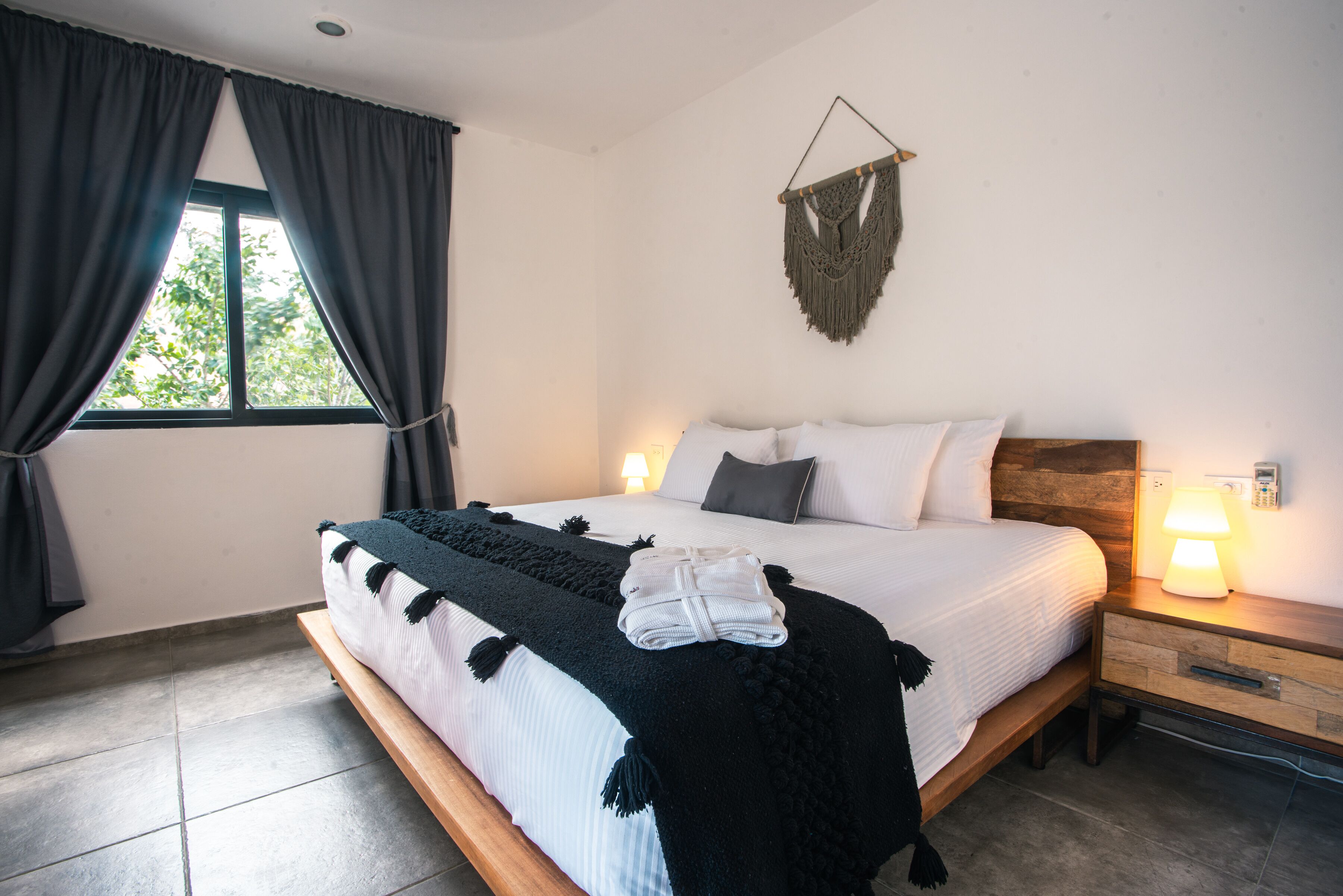 A neatly made bed with a black and white blanket, a wooden headboard, and a wall-mounted macrame piece.