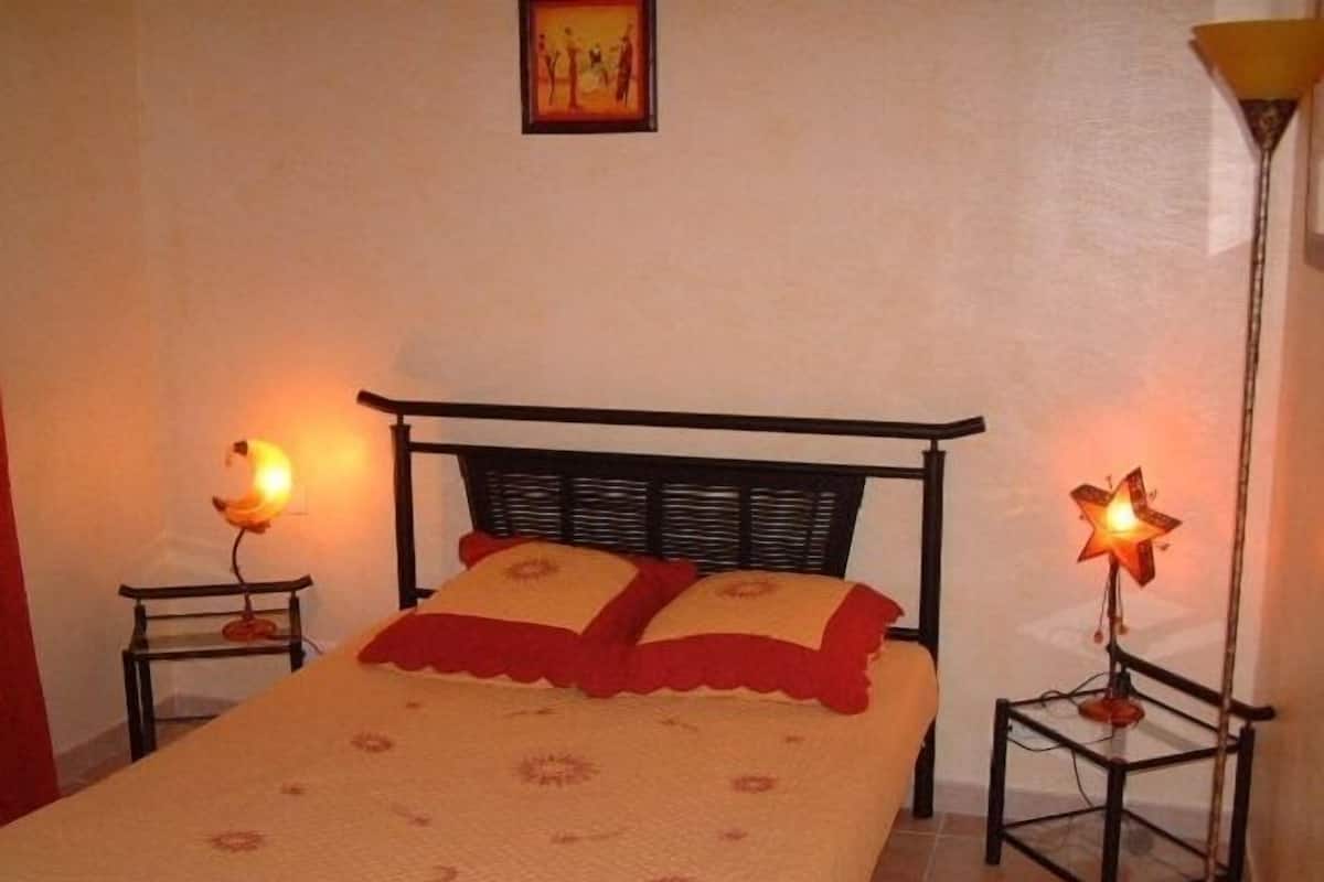 A bed with a patterned bedspread and two pillows, flanked by two bedside tables with lamps.