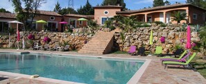 Zona de piscina amb mur de pedra, gandules i ombrelles.