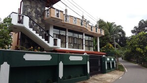 A two-story house with a stone facade, a red-tiled roof, and a green gate. - Basilico Homestay (Kegalle)