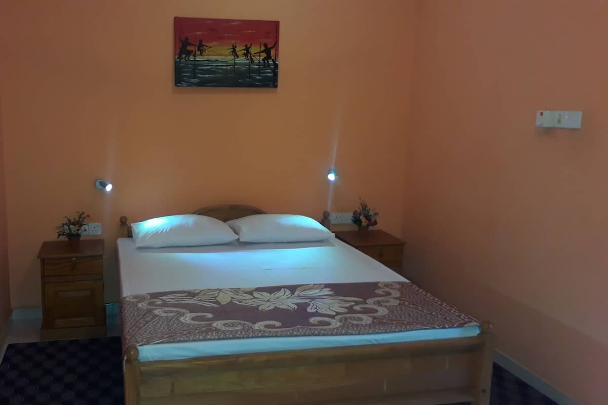 A bedroom with a bed, two bedside tables, a nightstand, a wall-mounted painting, and a wall socket.