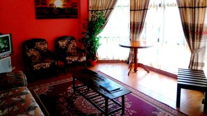 A living room with a red wall, two patterned armchairs, a wooden coffee table, a potted plant, and a small round table with a chair. - Basilico Homestay (Kegalle)