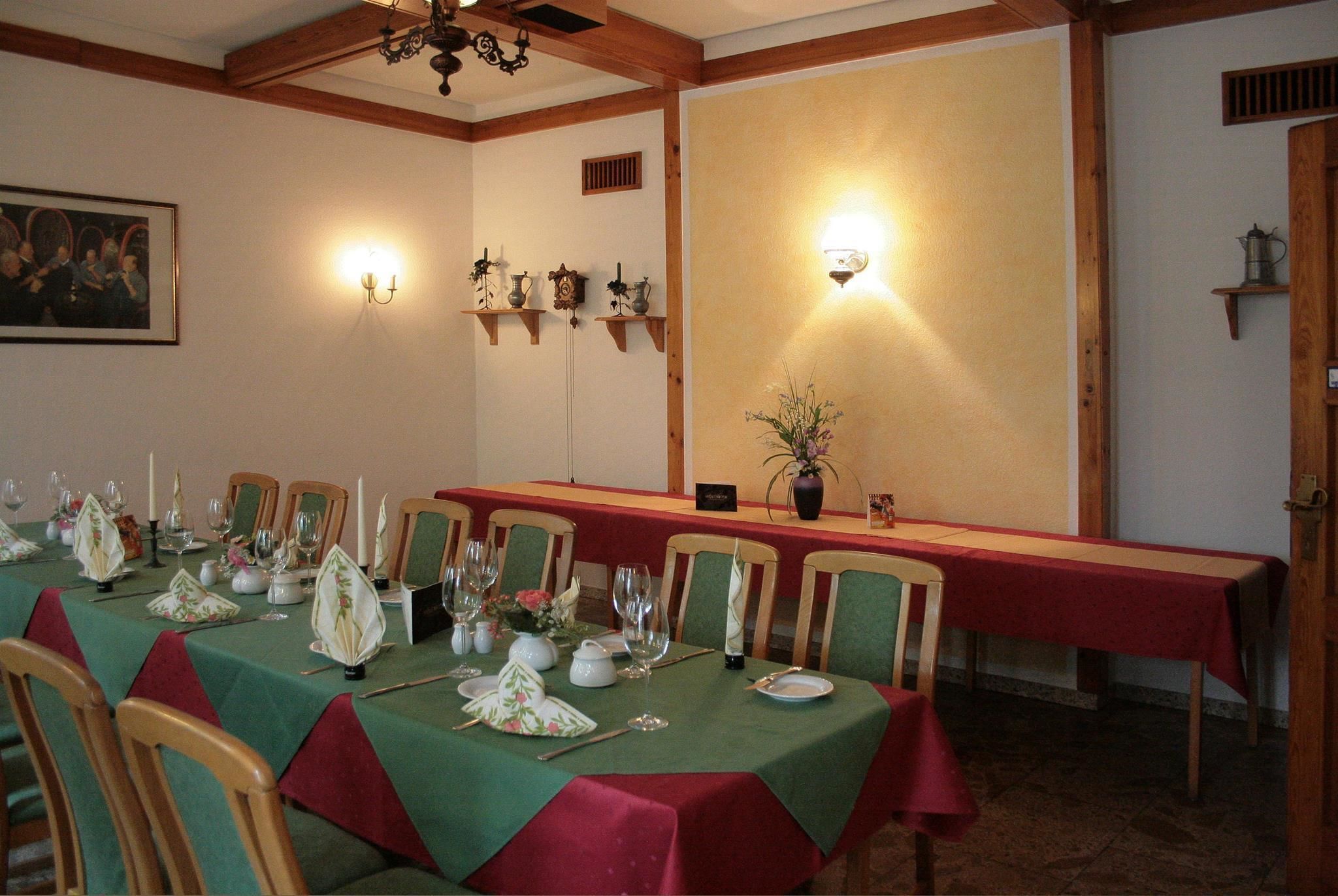 Un espace repas avec une longue table dressée pour le repas, des chaises en bois et des luminaires fixés au mur.