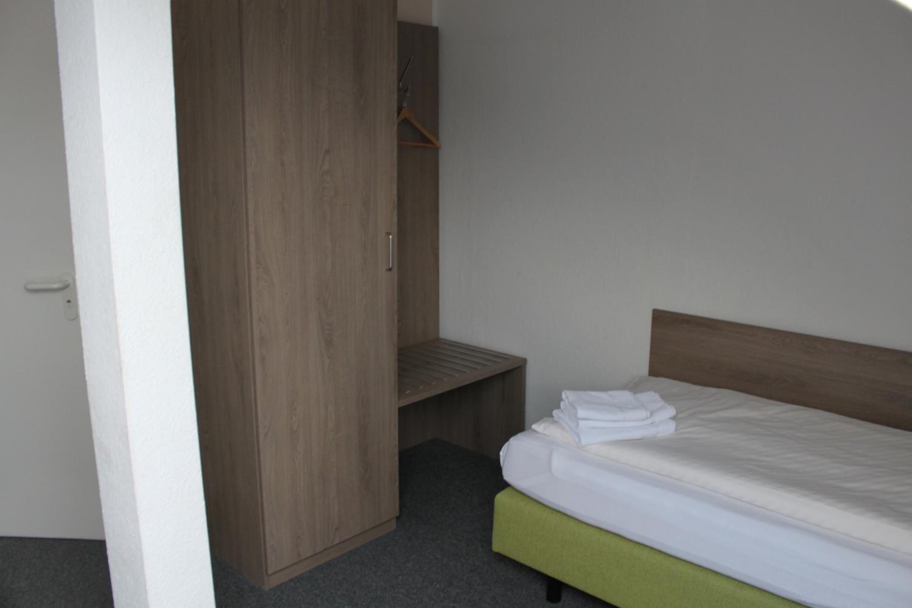 A bedroom with a wooden wardrobe, a green upholstered bed, and a small bench.
