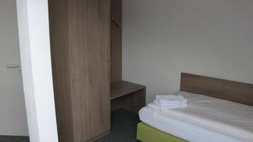 A bedroom with a wooden wardrobe, a green upholstered bed, and a small bench.