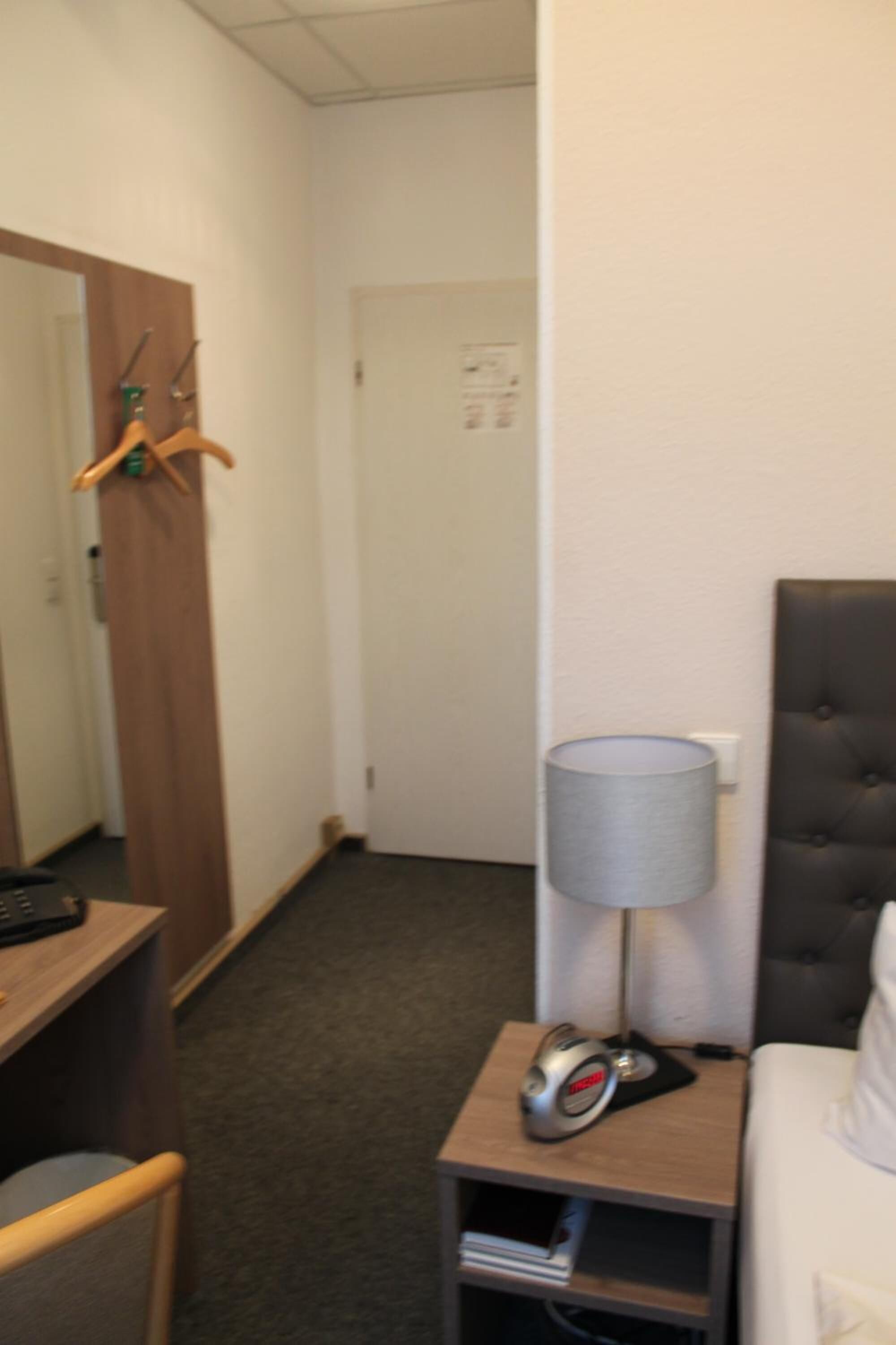 Una habitación de hotel con una cama, una mesita de noche con lámpara, una silla, un escritorio y una puerta.