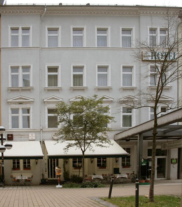 A hotel with a classical facade, multiple windows, and a covered entrance with outdoor seating.