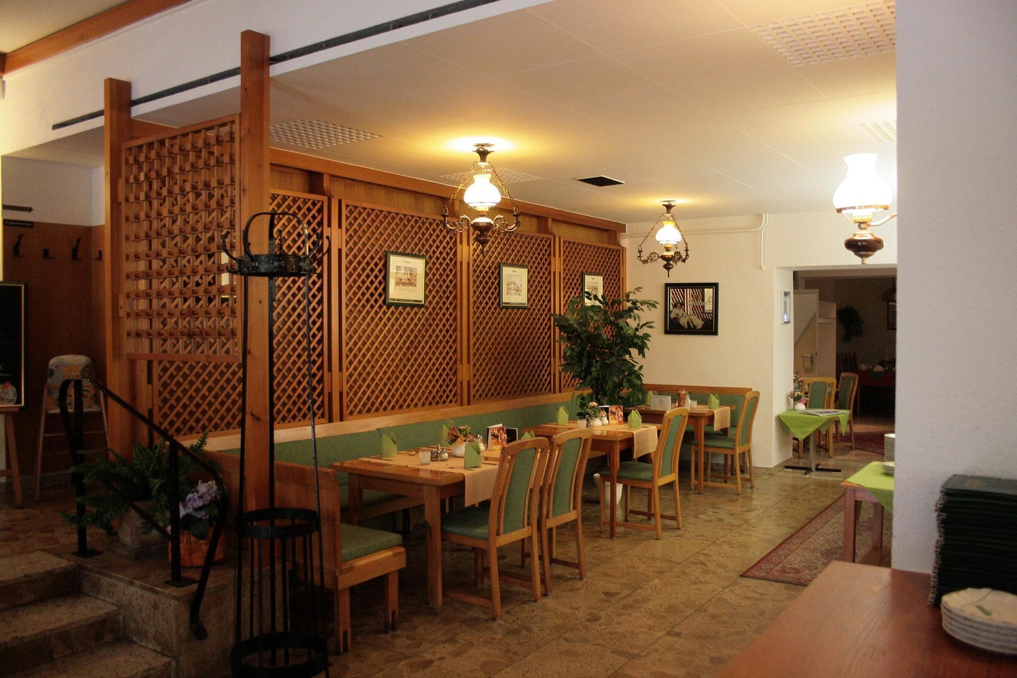 A restaurant with wooden furniture, green cushioned chairs, and a decorative wooden partition.