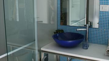 Un bagno con cabina doccia in vetro, lavabo blu, specchio e schienale piastrellato.