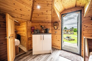 A wooden cabin interior with a kitchenette, a bathroom, and a door leading to an outdoor area.