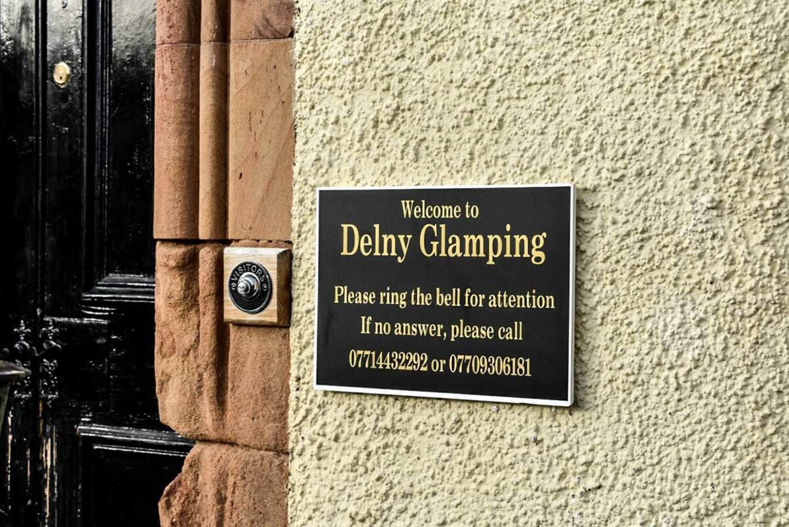 A welcome sign for Delny Glamping with contact numbers for assistance.