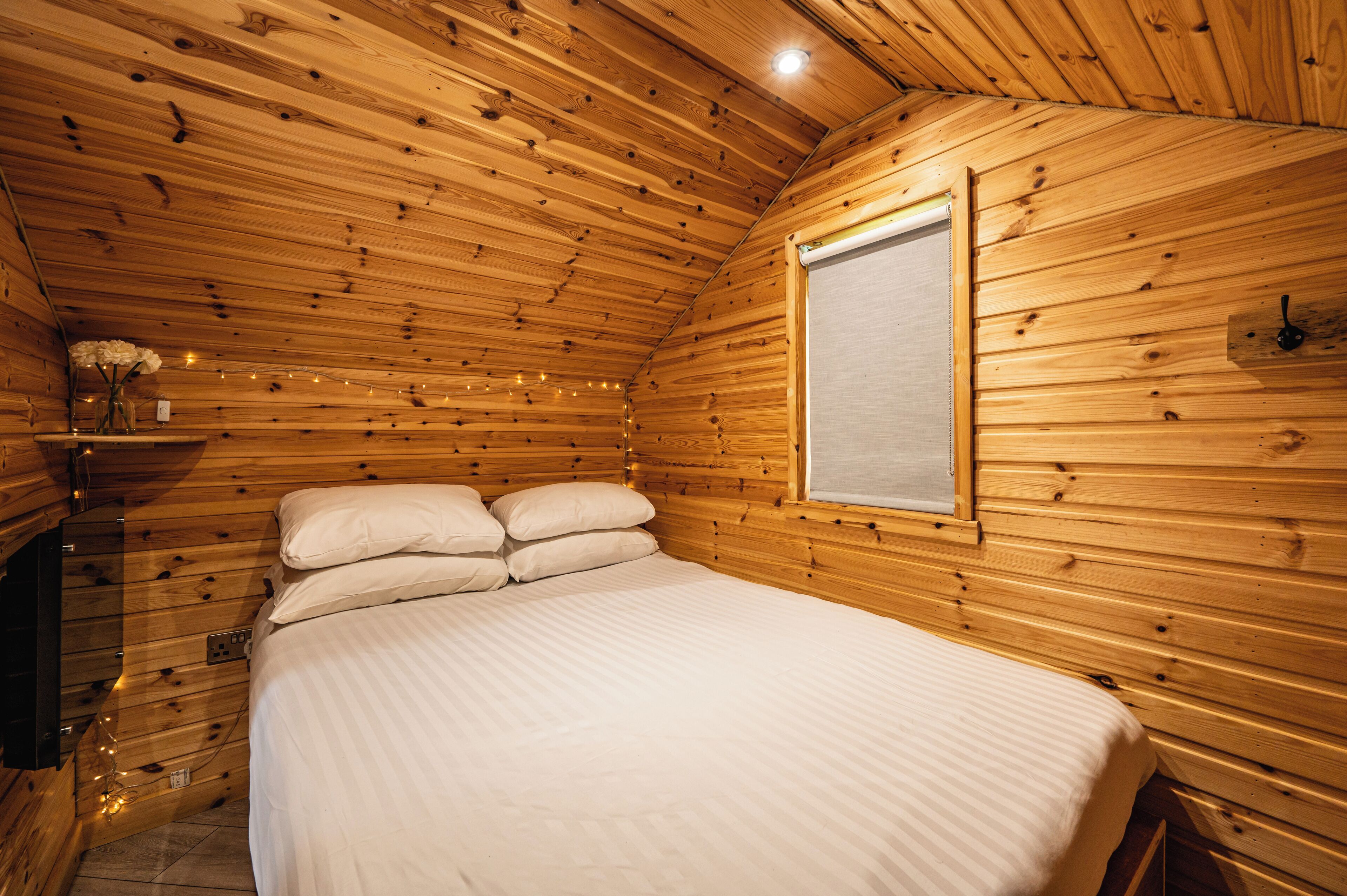 A wooden cabin bedroom with a bed, a window, and string lights.