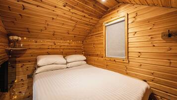 A wooden cabin bedroom with a bed, a window, and string lights.
