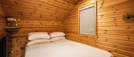A wooden cabin bedroom with a bed, a window, and string lights.