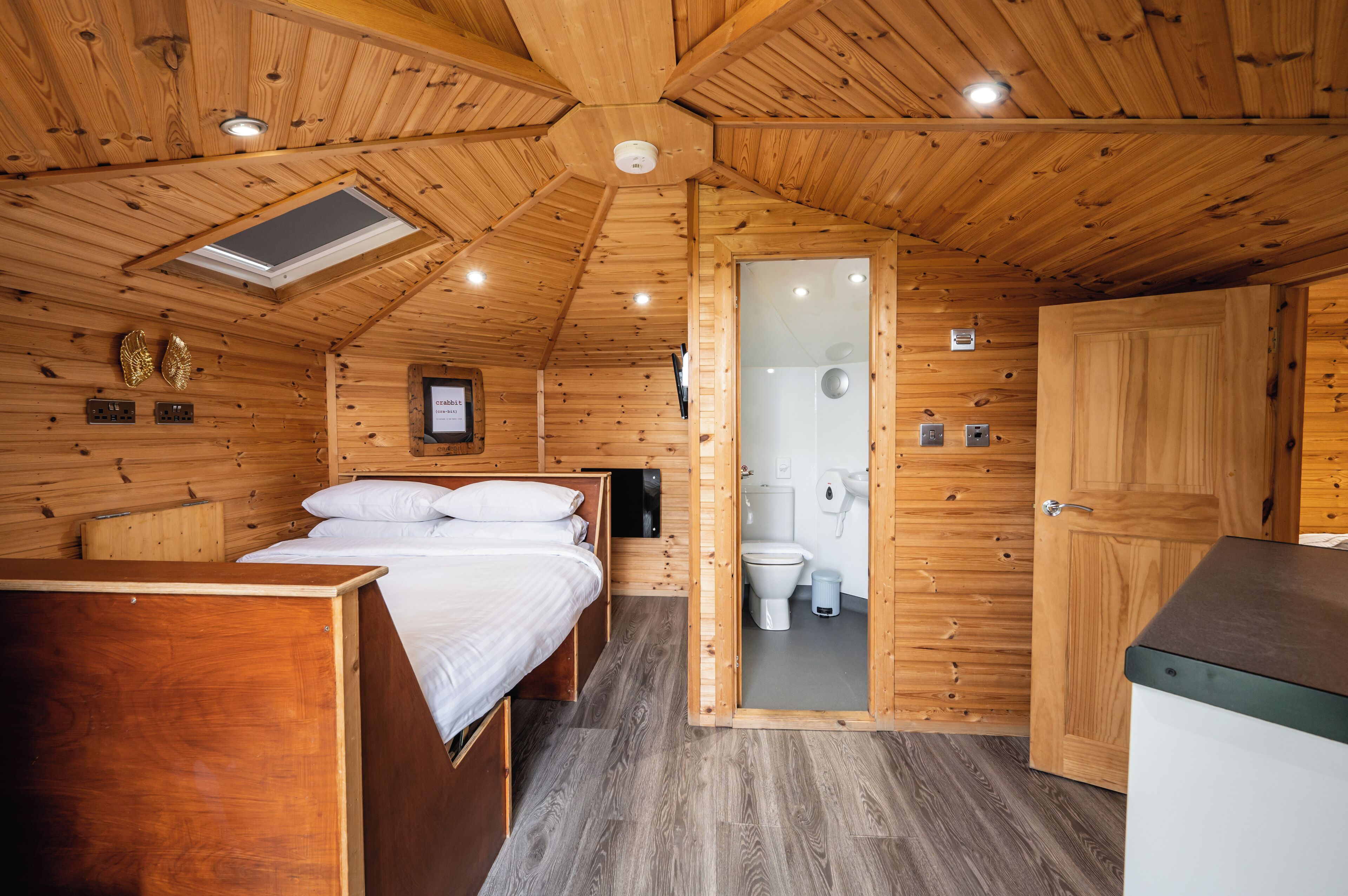 Uma cabana de madeira com uma cama de solteiro, banheiro e cozinha compacta.
