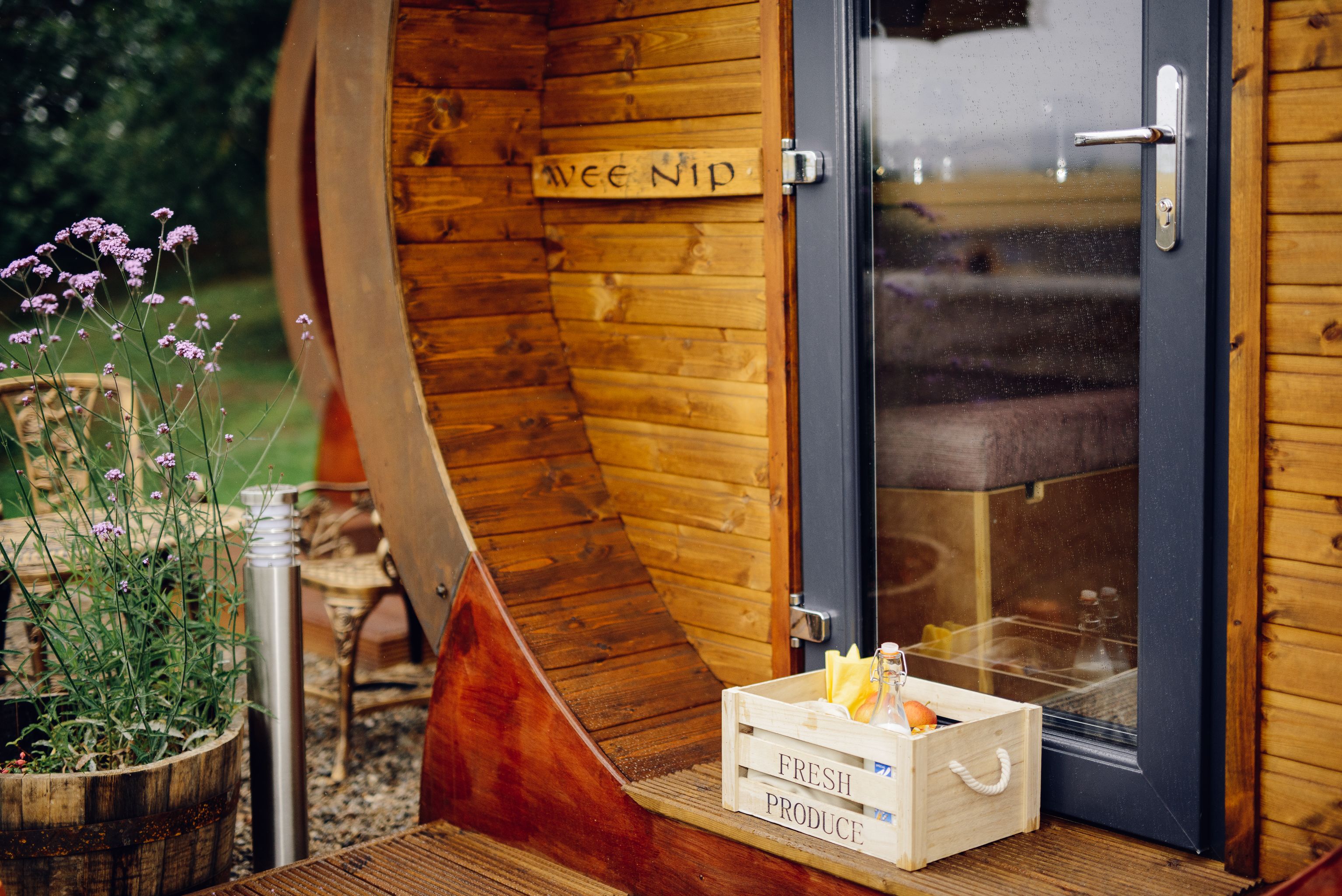 Una cabaña de madera con una puerta que dice "Wee NIP". Un fardel de madera con la leyenda "FRESH PRODUCE" está colocado afuera.