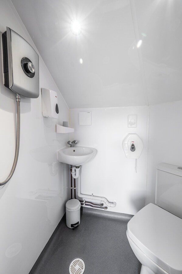 A modern bathroom with a white sink, toilet, and shower. - Delny Glamping (Invergordon)