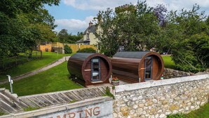 A glamping site with two wooden barrel-style cabins, a stone wall, and a grassy area with trees. - Delny Glamping (Invergordon)