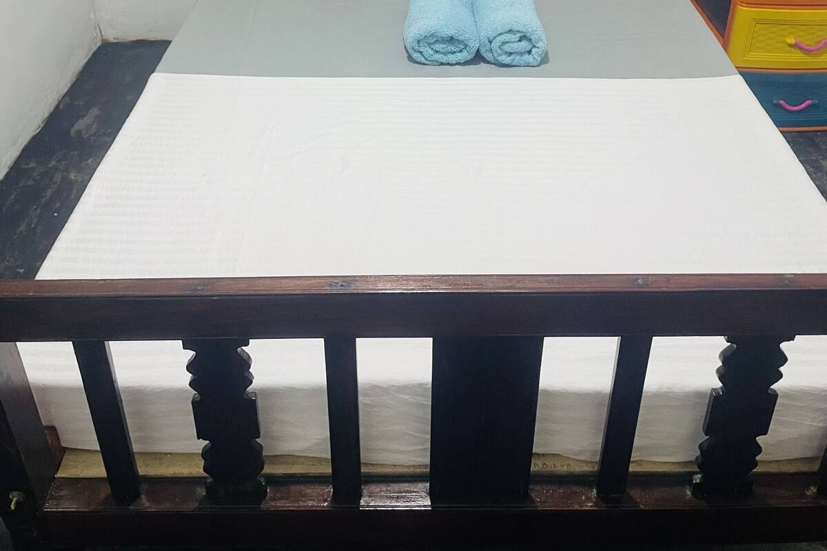 Una cama con ropa de cama blanca y azul, dos toallas enrolladas y un cabecero de madera.