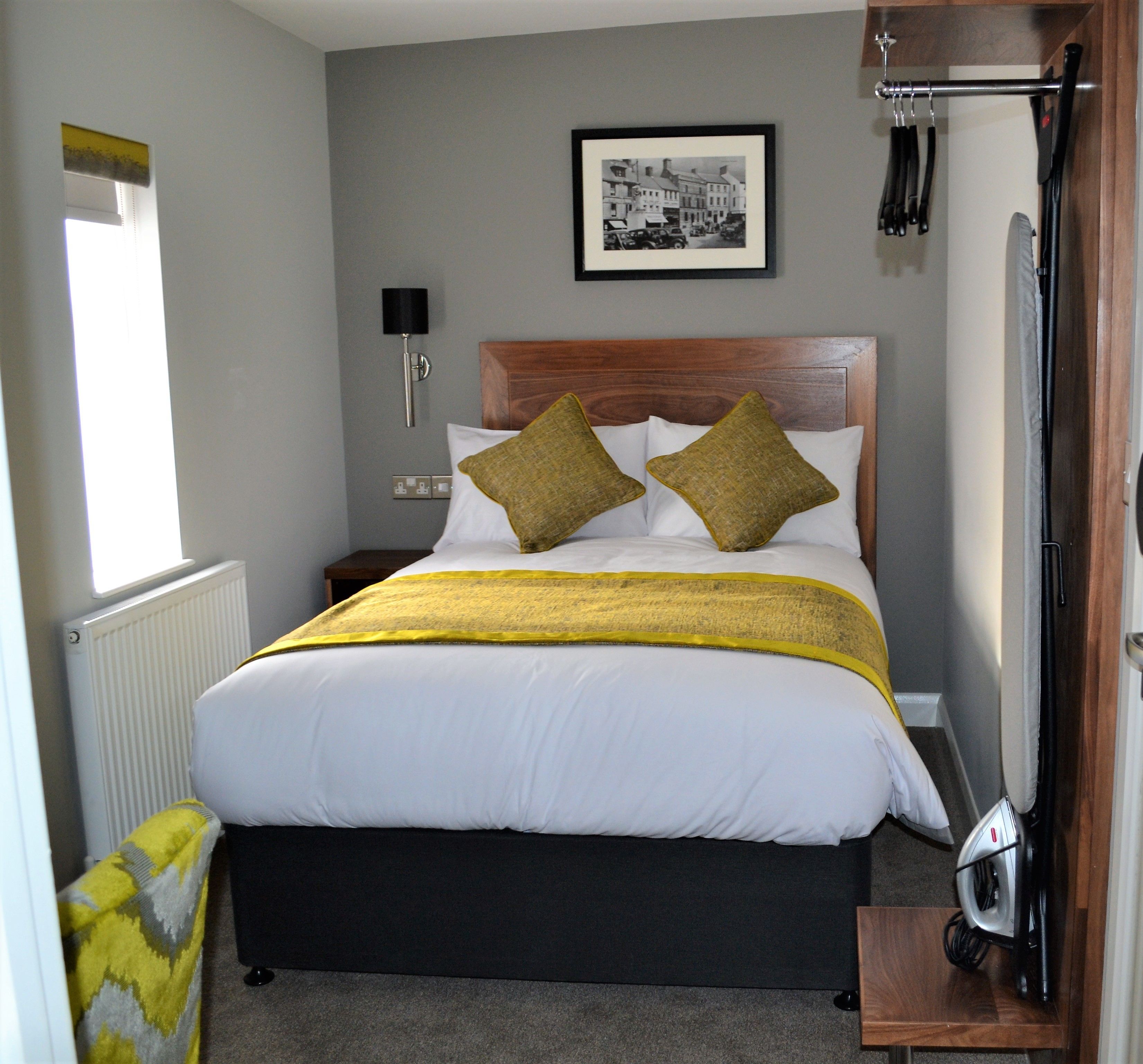 A neatly arranged hotel room with a bed, a framed picture on the wall, a radiator, and a window.
