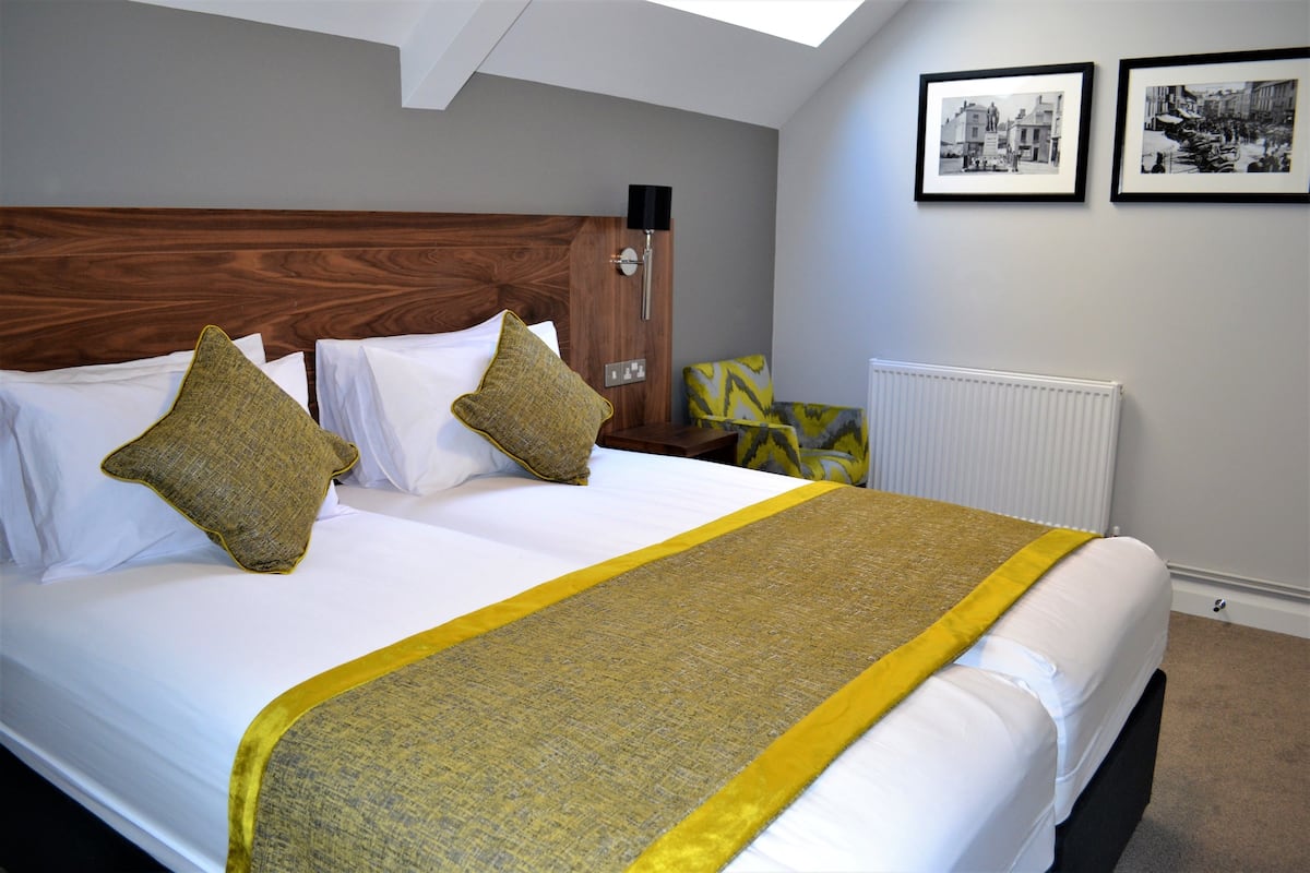 Een keurig opgemaakt bed met een houten hoofdbord, witte beddengoed en decoratieve kussens.