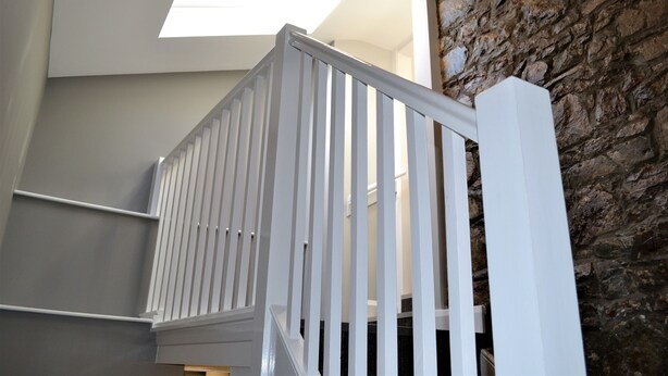 Un escalier avec des rampes blanches et un mur en pierre.