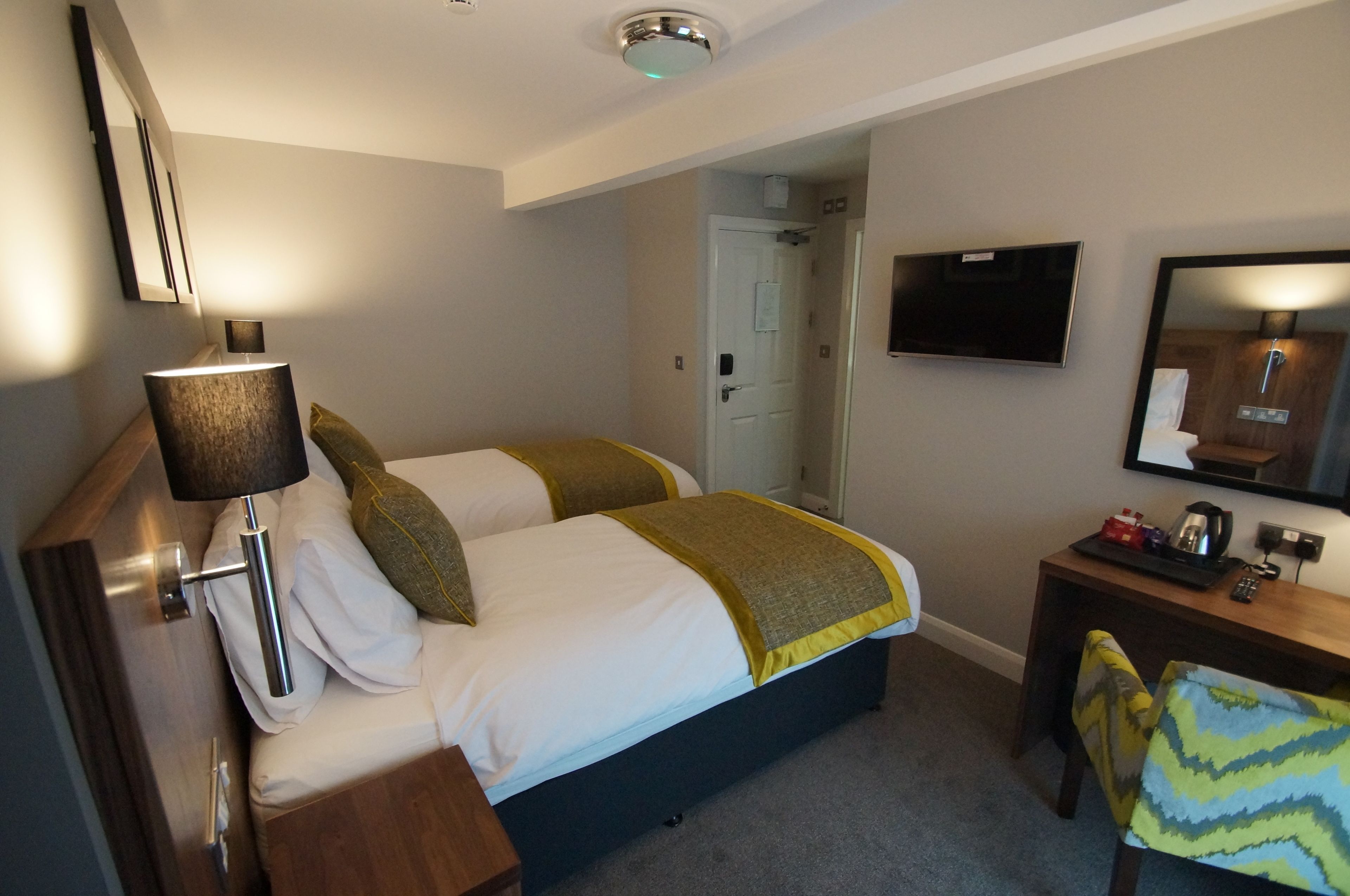 Una habitación de hotel con dos camas, un escritorio, una silla, un televisor y un espejo.