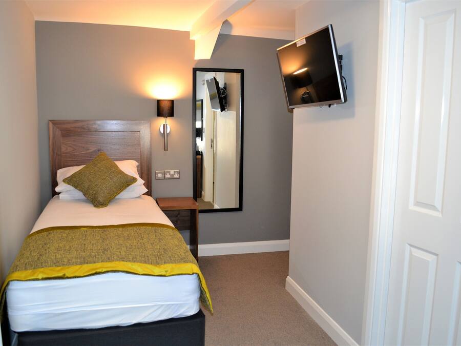 A hotel room with a bed, a bedside table, a mirror, a TV mounted on the wall, and a door.
