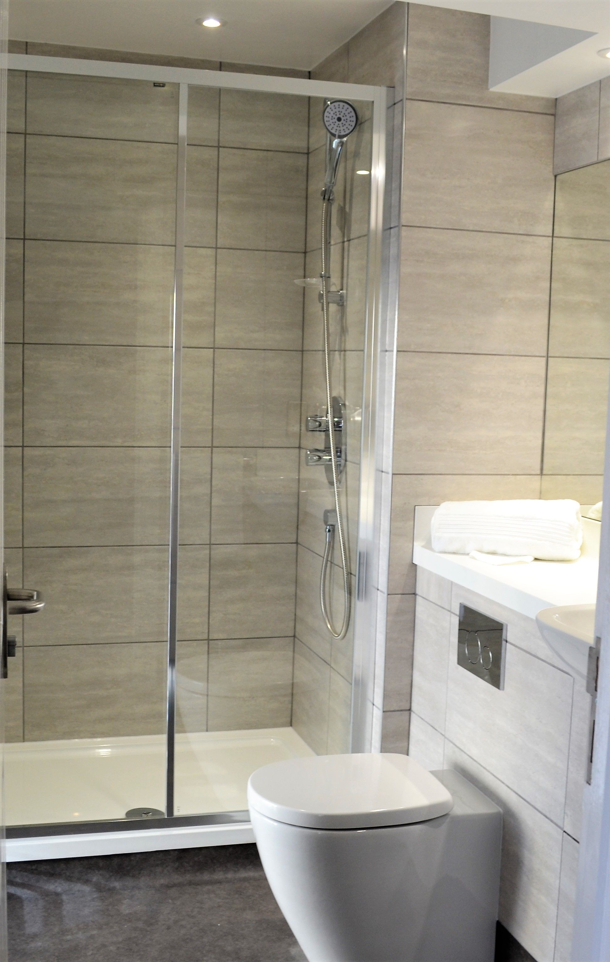 A modern bathroom with a glass-enclosed shower, a white toilet, and a vanity with a towel.