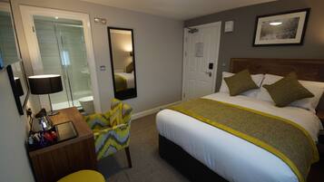 A hotel room with a bed, a desk with a lamp, a chair, a mirror, and a shower.
