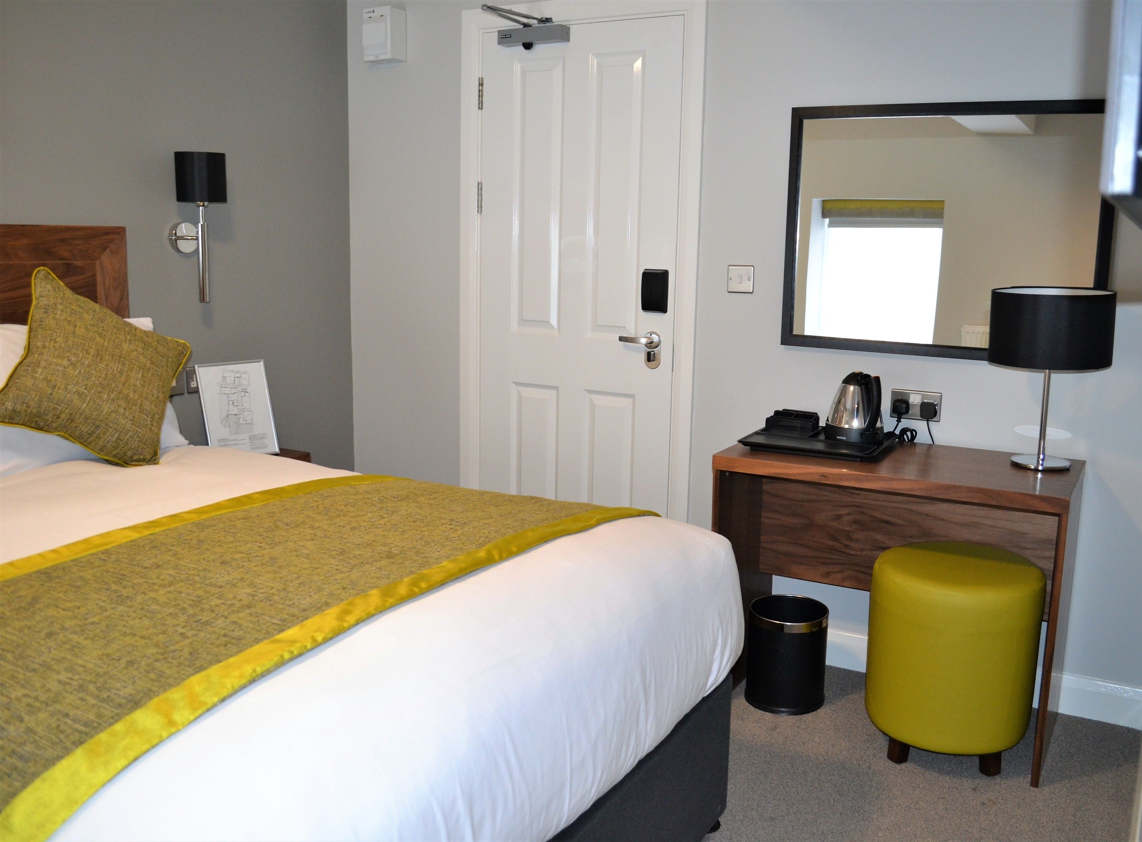 Habitación de hotel con cama, escritorio, silla, cesto de basura, espejo y lámpara.