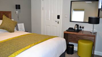 Habitación de hotel con cama, escritorio, silla, cesto de basura, espejo y lámpara.