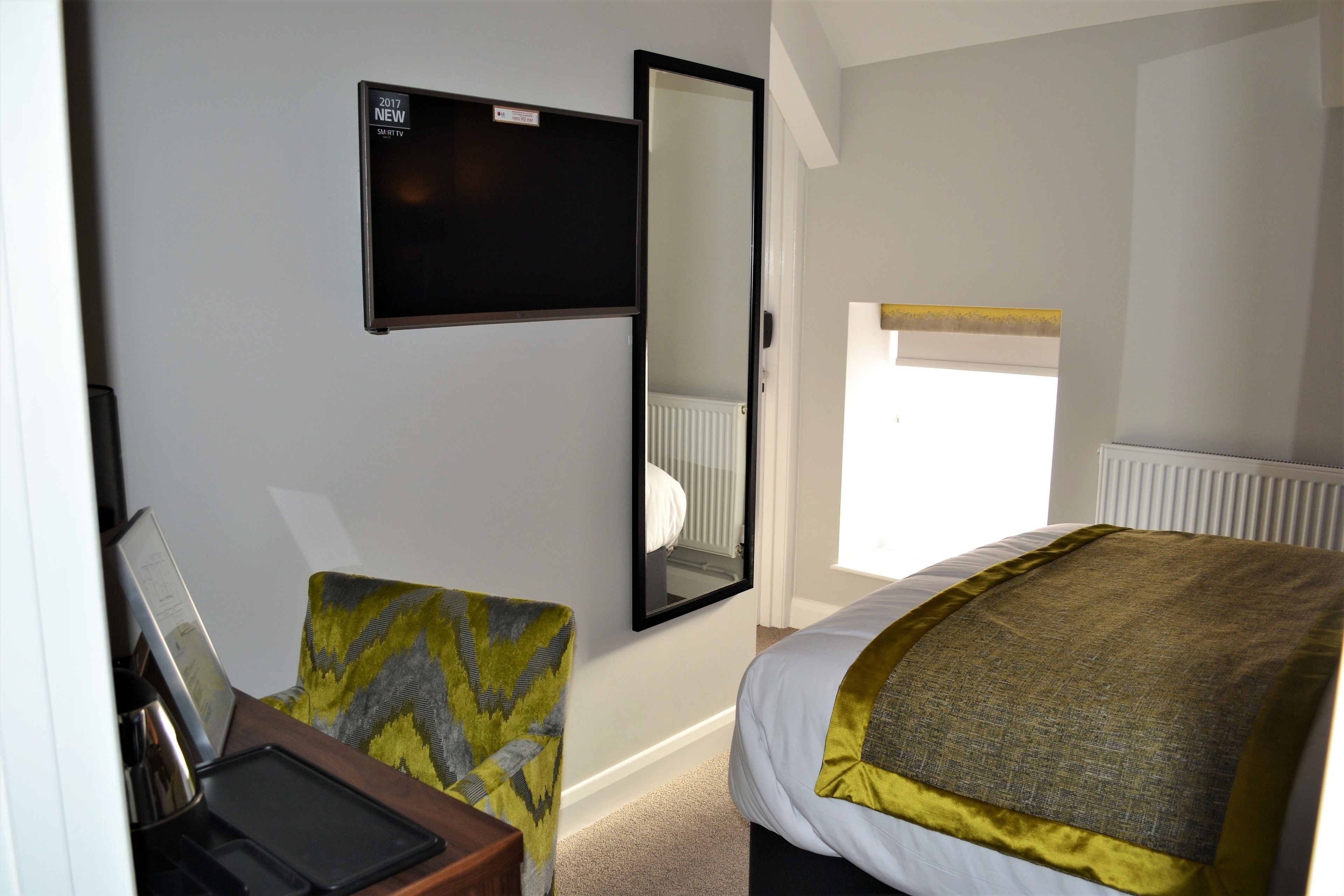 Quarto de hotel com cama, cadeira, escrivaninha, TV de tela plana e janela.
