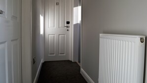 Un couloir étroit avec une porte blanche portant le numéro 10, un radiateur blanc sur le côté droit et un sol recouvert d’une moquette sombre.