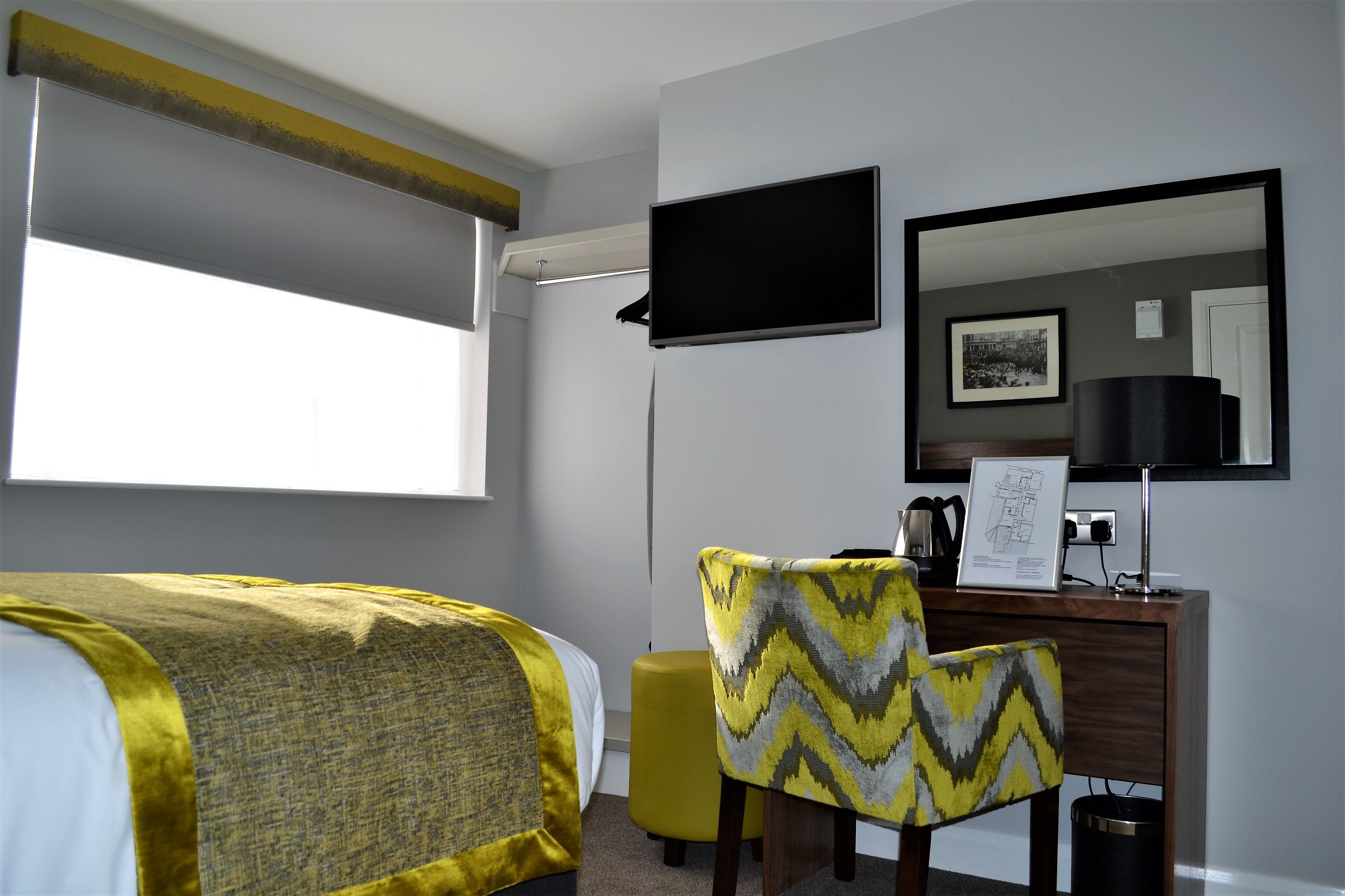 Una habitación de hotel con cama, escritorio, silla, televisor y ventana.
