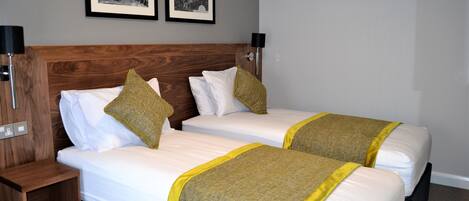 A hotel room with two beds, a wooden headboard, and two framed pictures on the wall.