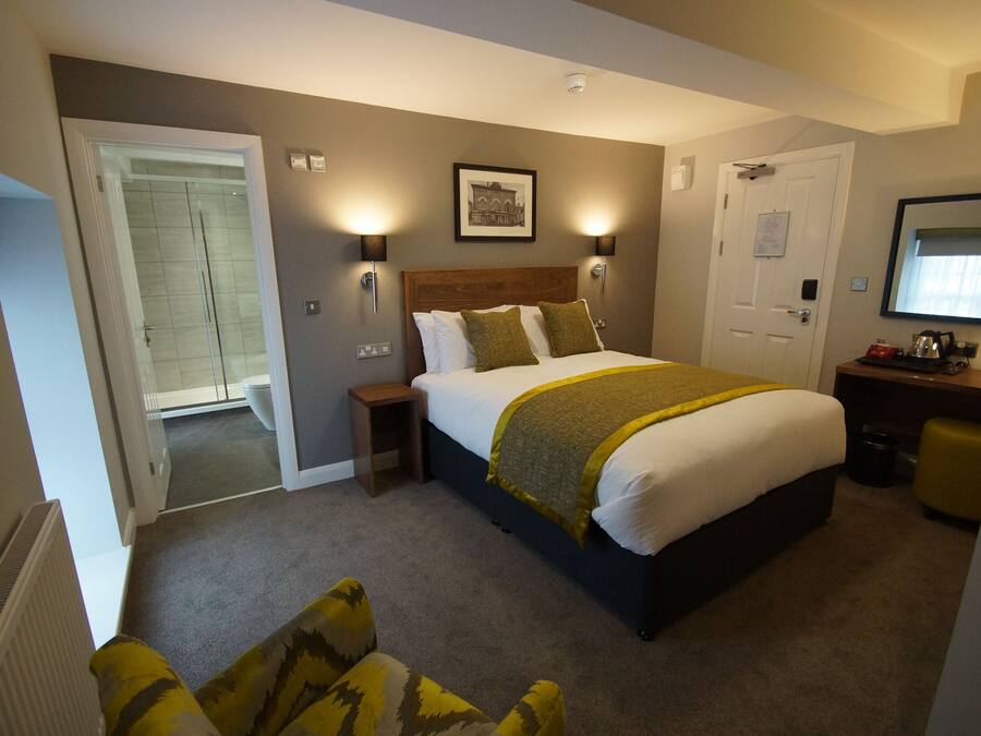 A hotel room with a large bed, bedside lamps, a small table, a mirror, and a door leading to a bathroom.