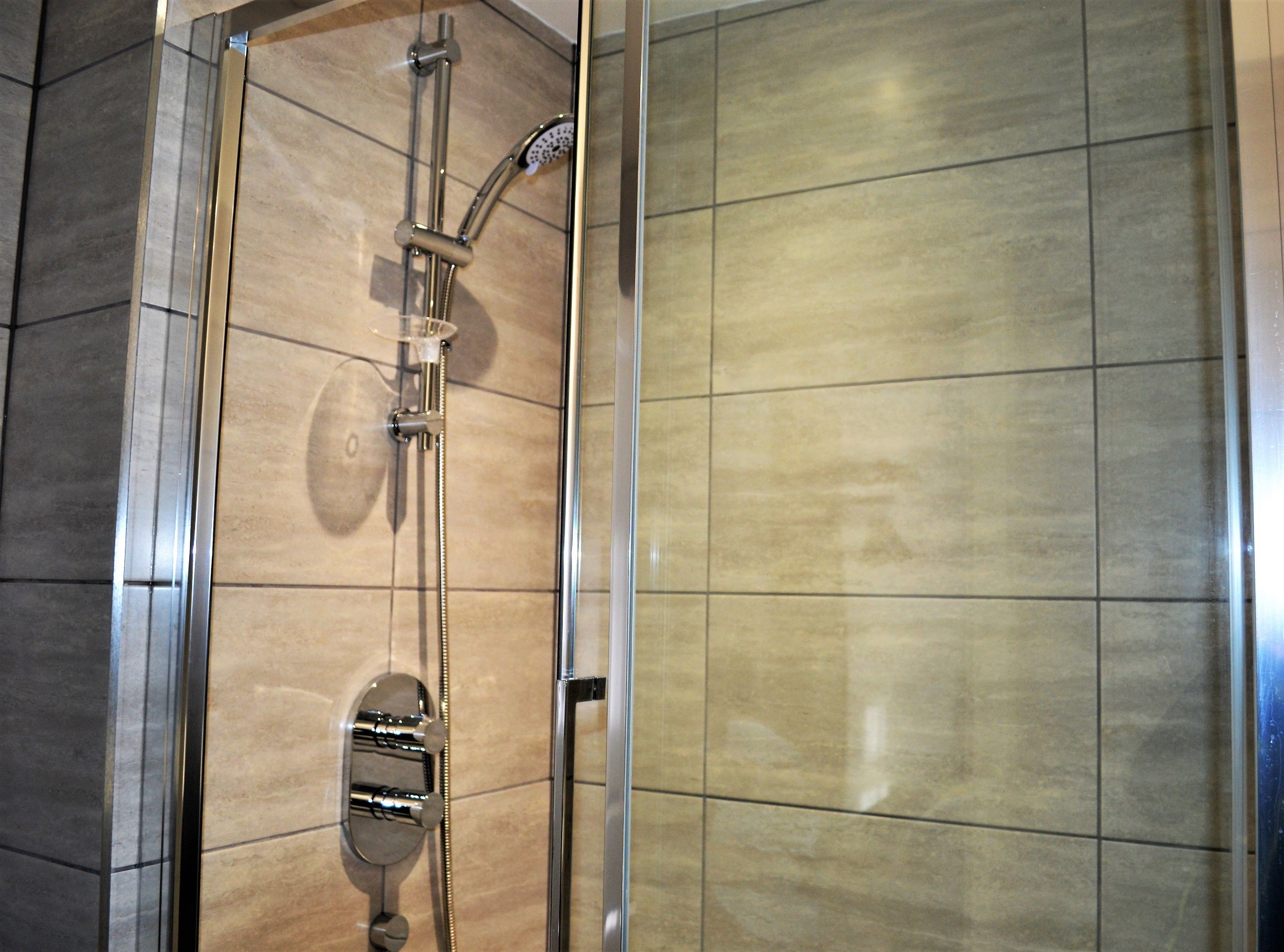 Eine Dusche mit Handbrause und Bedienfeld an der Wand.
