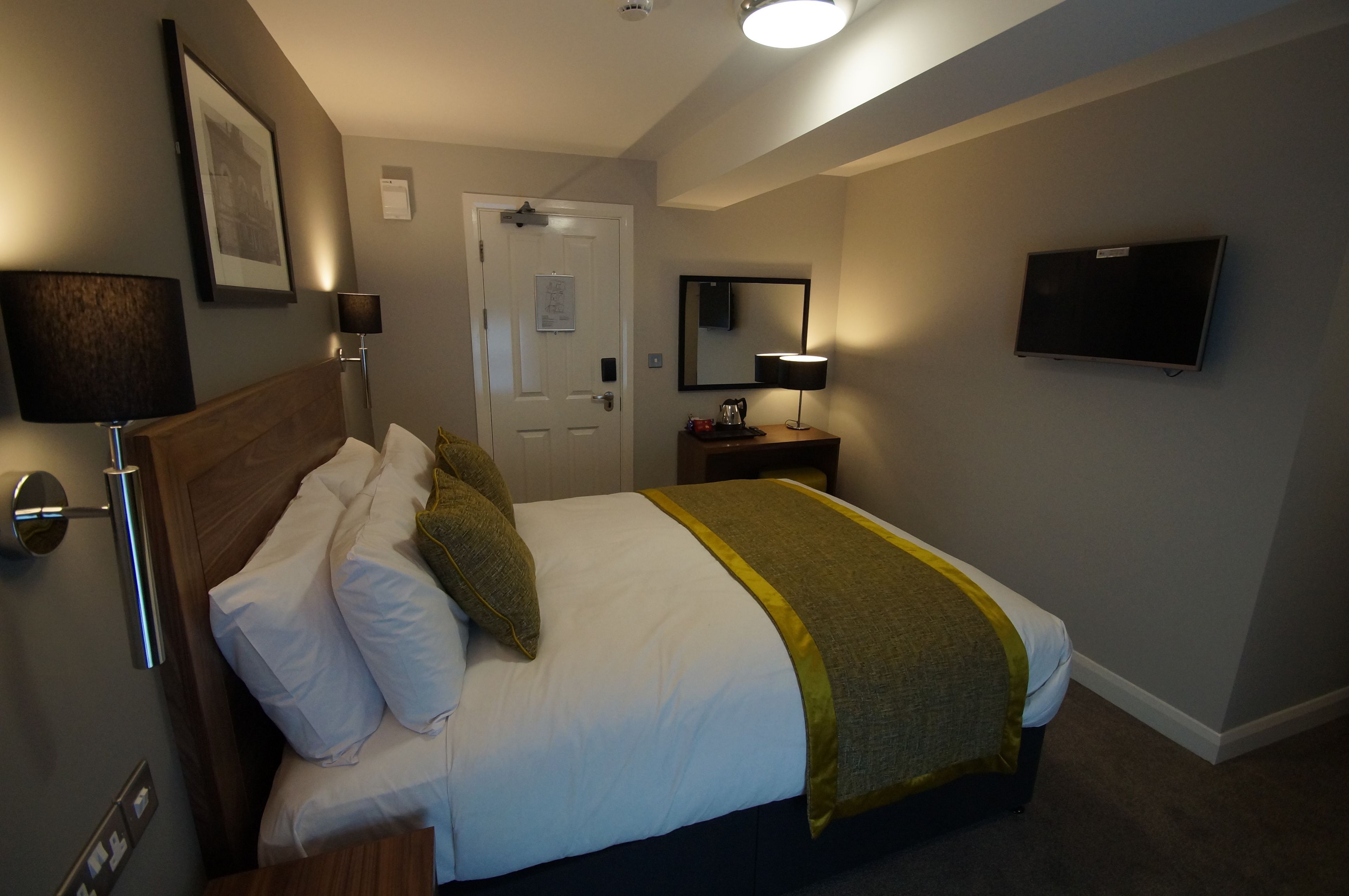 A hotel room with a bed, bedside lamps, a TV, and a door.