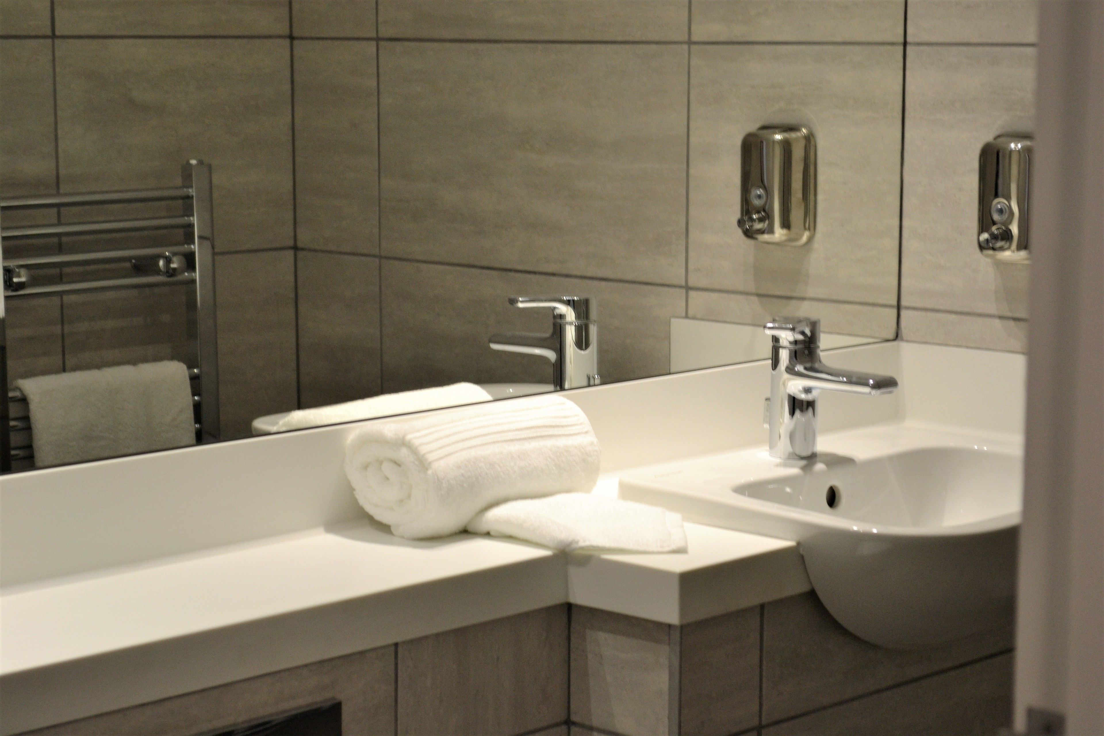 Un baño moderno con un lavamanos blanco, un espejo y un perchero para toallas.
