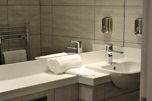 Un baño moderno con un lavamanos blanco, un espejo y un perchero para toallas.