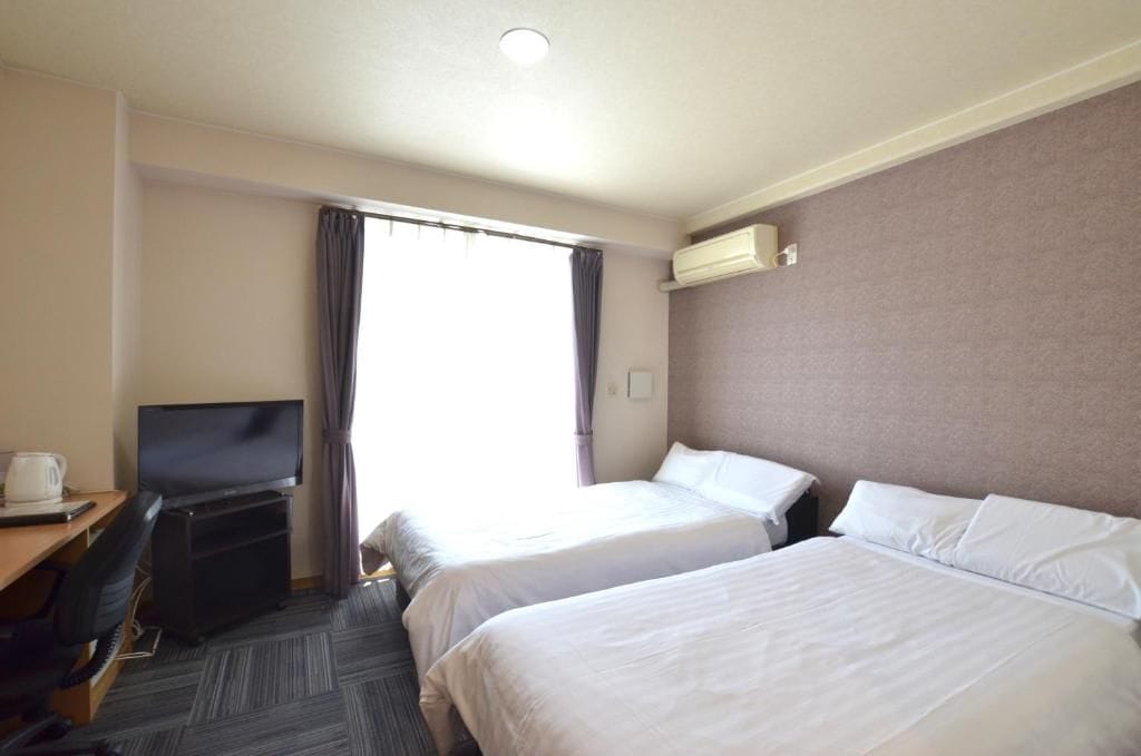 Une chambre d’hôtel avec deux lits, un bureau avec une télévision et un appareil de climatisation.