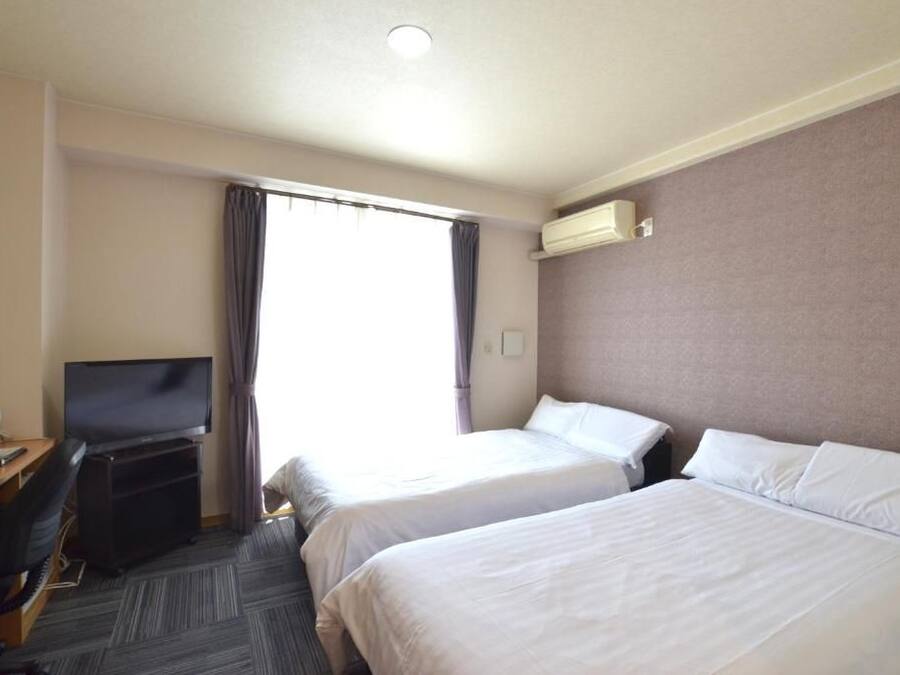 Une chambre d’hôtel avec deux lits, un bureau avec une télévision et un appareil de climatisation.
