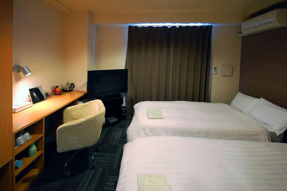 A hotel room with two beds, a desk with a computer, a chair, a television, and a window with curtains.