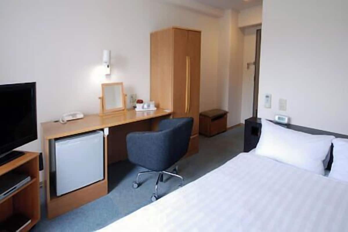 A hotel room with a bed, a desk with a computer, a TV, and a small fridge.
